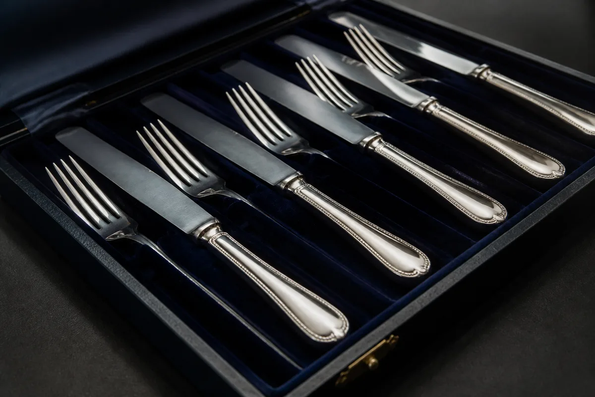 Coffret ouvert contenant des couverts en argent alignés sur un velours sombre, lumière rasante